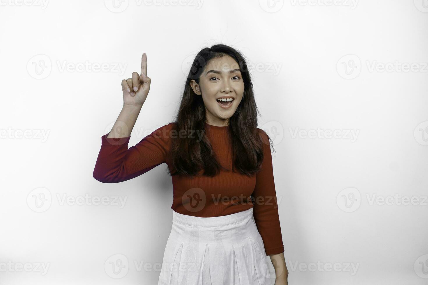 excité asiatique femme portant rouge T-shirt, montrer du doigt à le copie espace sur Haut de son, isolé par blanc Contexte photo