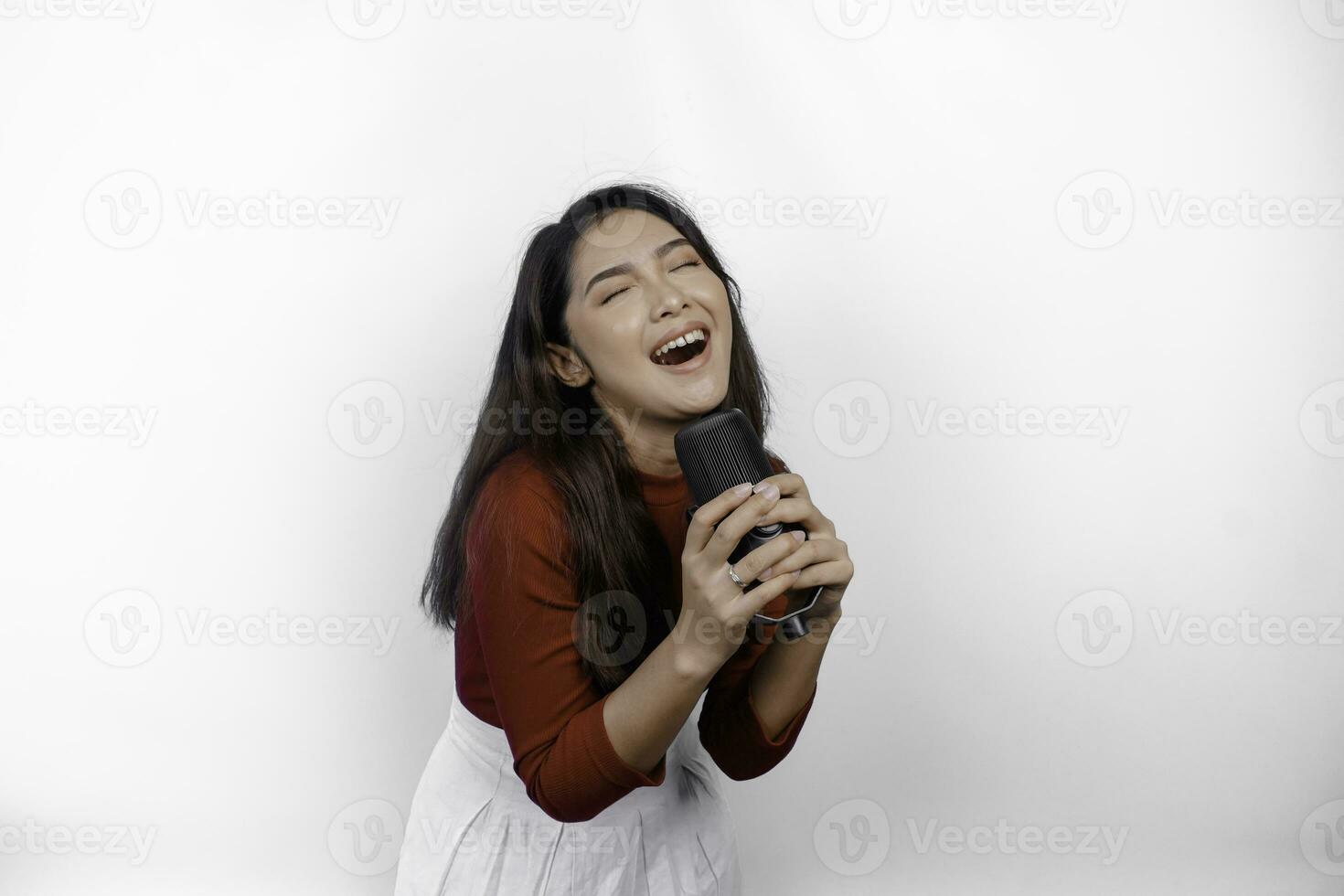 portrait d'une femme asiatique insouciante, s'amusant au karaoké, chantant au microphone en se tenant debout sur fond blanc photo