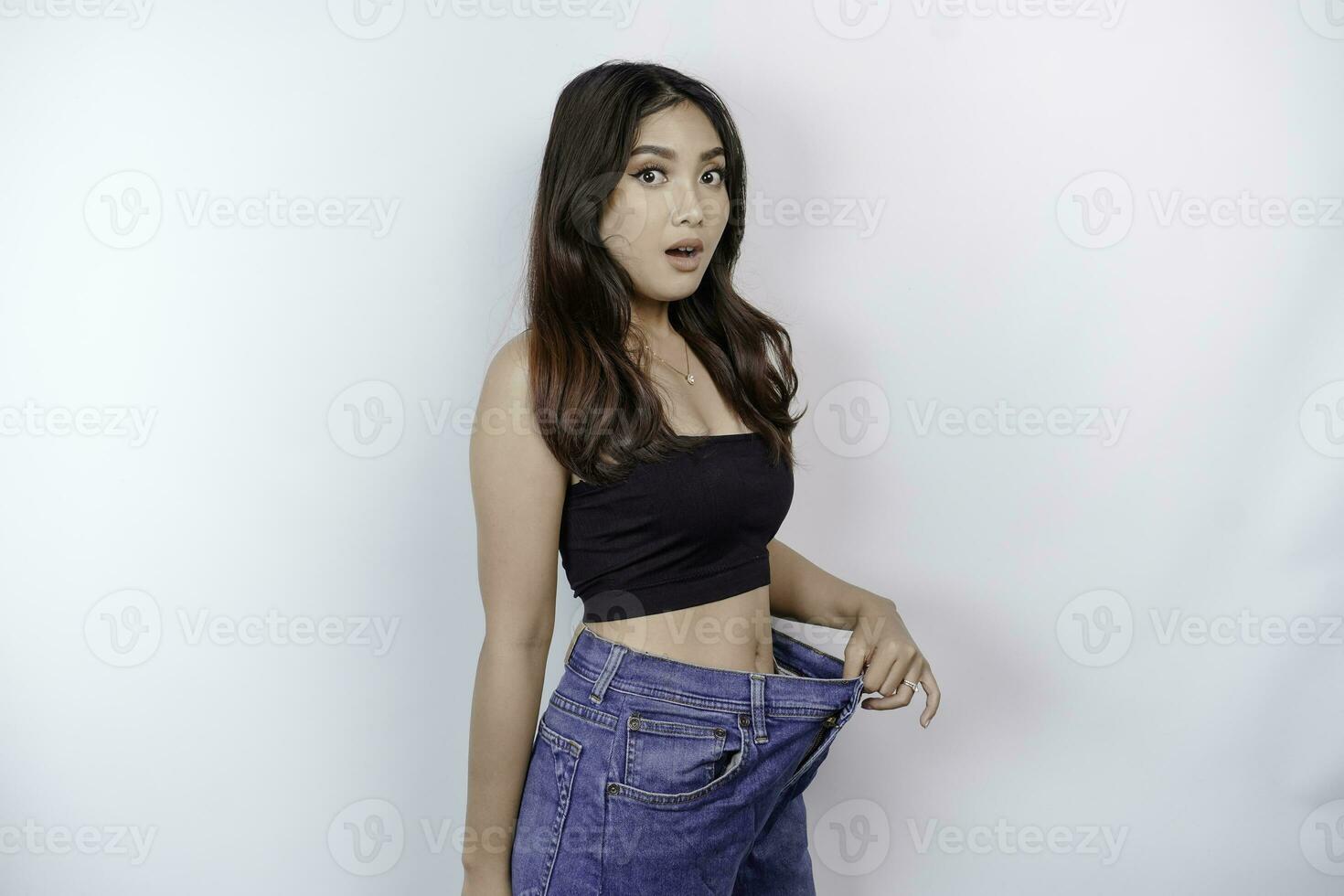 régime et poids perte concept. une Jeune asiatique femme dans énorme jeans isolé sur une blanc Contexte. photo