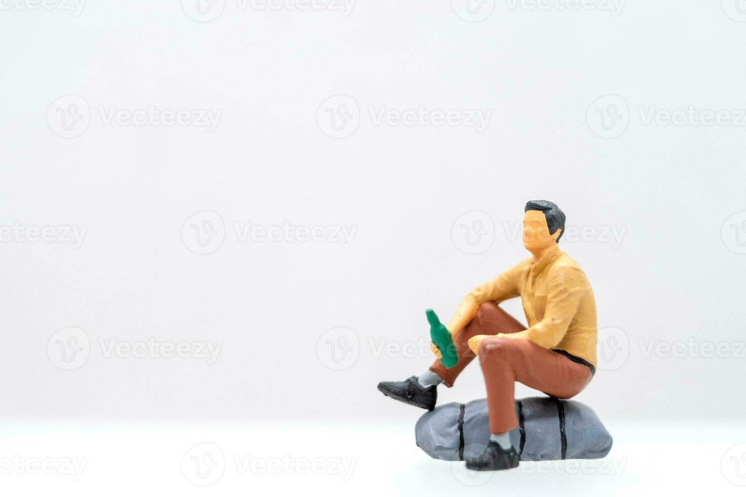 miniature gens Jeune homme séance sur une Roche tandis que agrippant une l'eau bouteille. photo