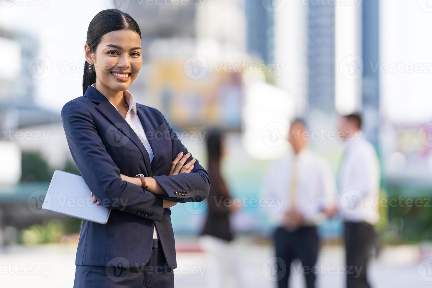 portrait d'une femme d'affaires souriante, les bras croisés en se tenant devant des immeubles de bureaux modernes photo
