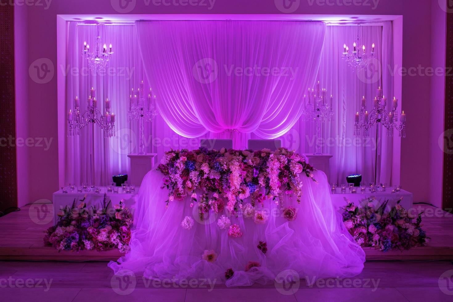 table de fête pour les mariés décorée de tissu, de chandelier et de fleurs. décoration de mariage avec lumière violette photo