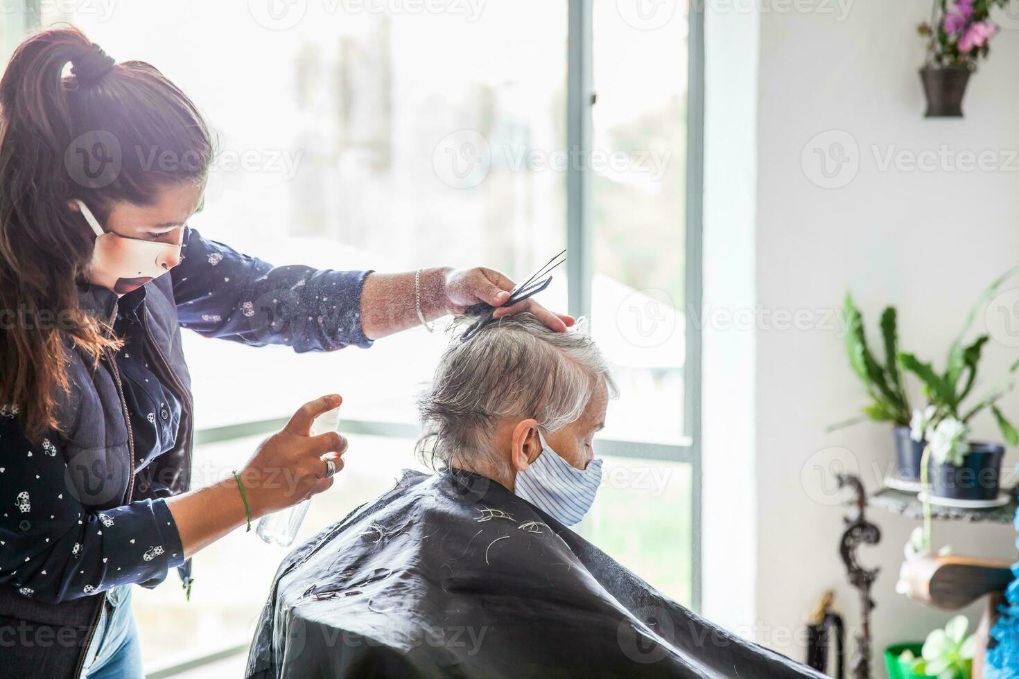 Sénior femme avoir une la Coupe de cheveux à Accueil pendant covid19 pandémie portant visage masque photo