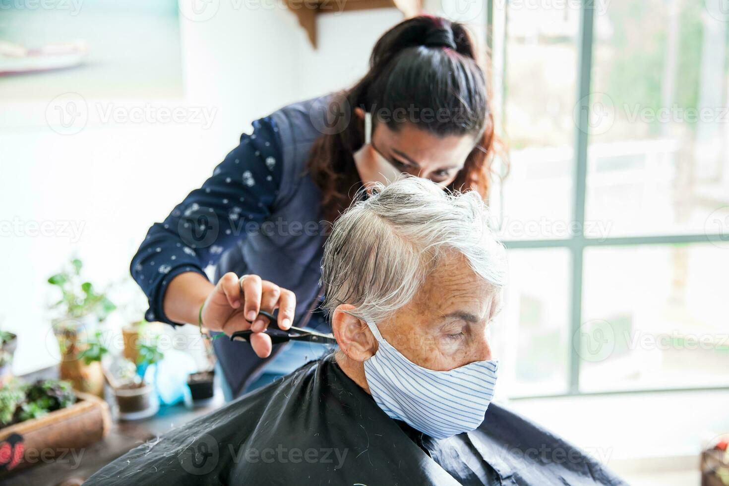 Sénior femme avoir une la Coupe de cheveux à Accueil pendant covid19 pandémie portant visage masque photo