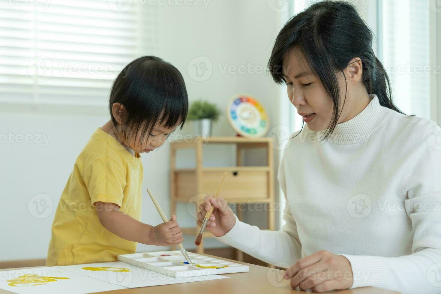 content Asie mère en jouant apprentissage peindre pour peu fille. marrant famille est content et excité dans le maison. mère et fille ayant amusement dépenses temps ensemble. vacances, activité photo
