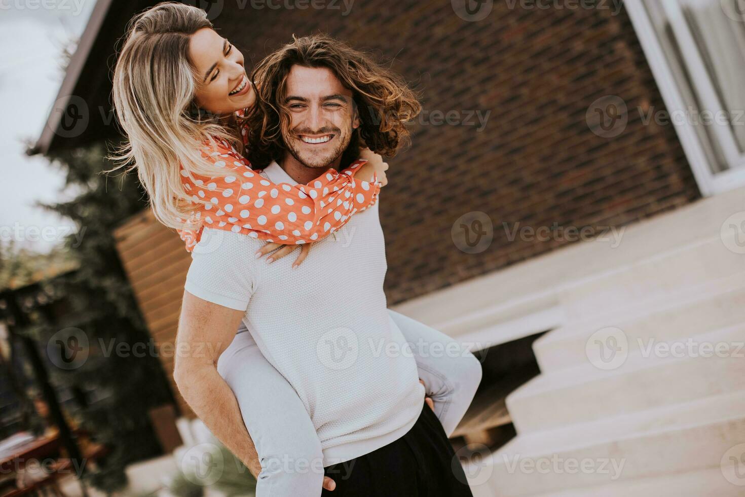 Beau longue cheveux homme porter le Jeune femme sur le sien retour dans de face de brique maison photo