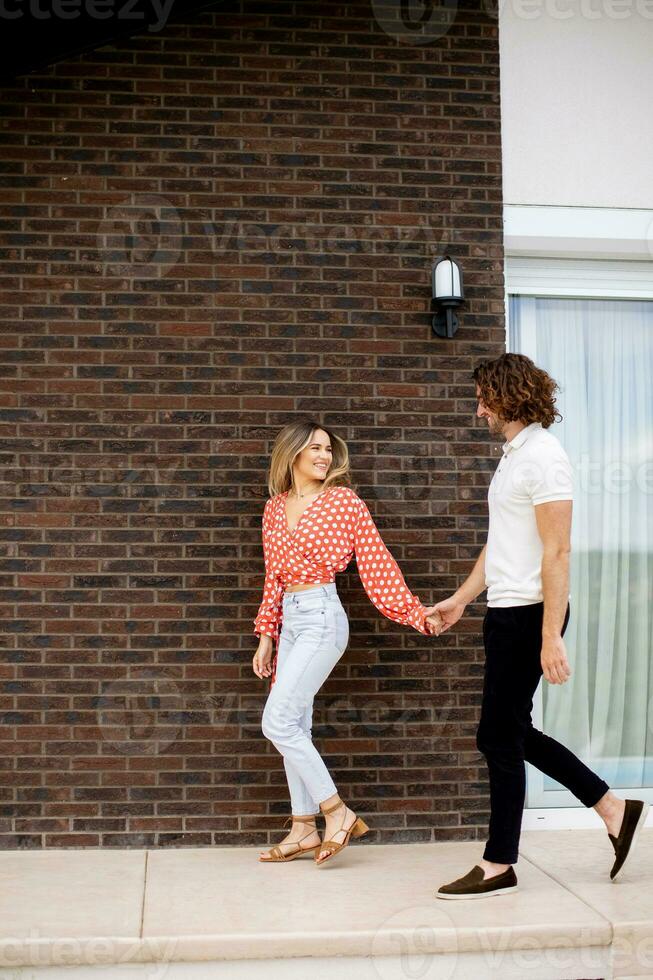 souriant Jeune couple dans l'amour en marchant dans de face de maison brique mur photo