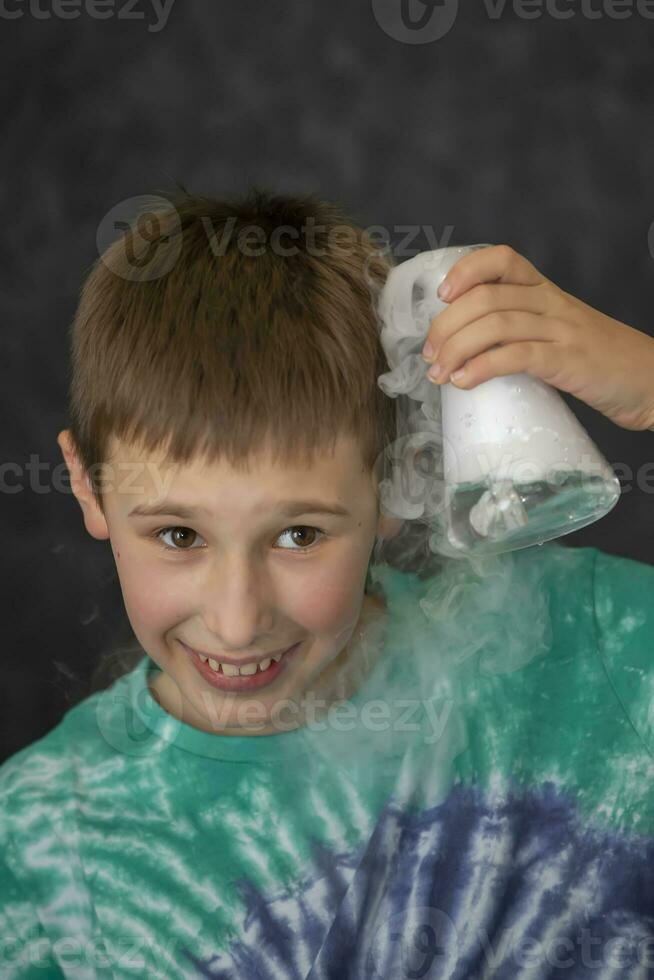 une garçon conduit une scientifique chimique expérience avec liquide azote. une enfant avec une verre ballon rempli avec fumée. photo