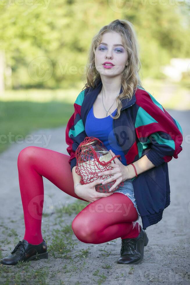 une magnifique Années 90 pays fille dans brillant vêtements détient une chaîne sac avec une pouvez de bouleau sève. russe femme dans le style de le années 90. photo