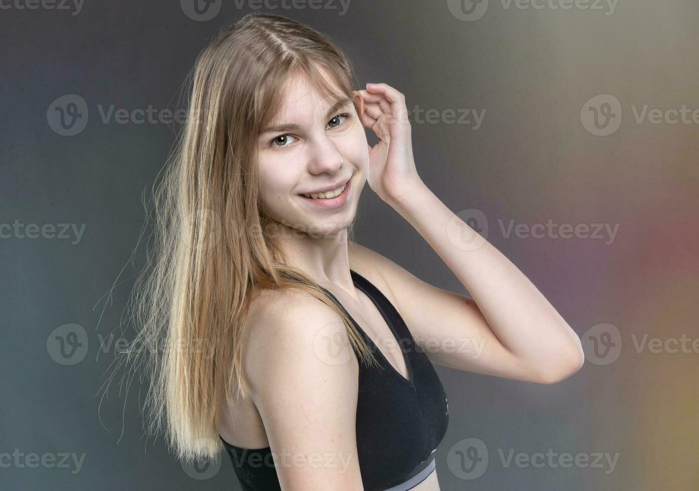 une magnifique adolescent fille dans une des sports maillot de corps sur une gris Contexte regards à le caméra et sourit. photo