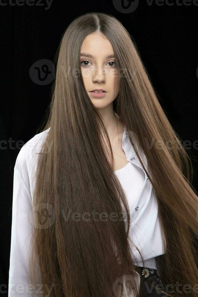verticale portrait de une magnifique fille avec très longue luxueux cheveux sur une foncé Contexte. photo