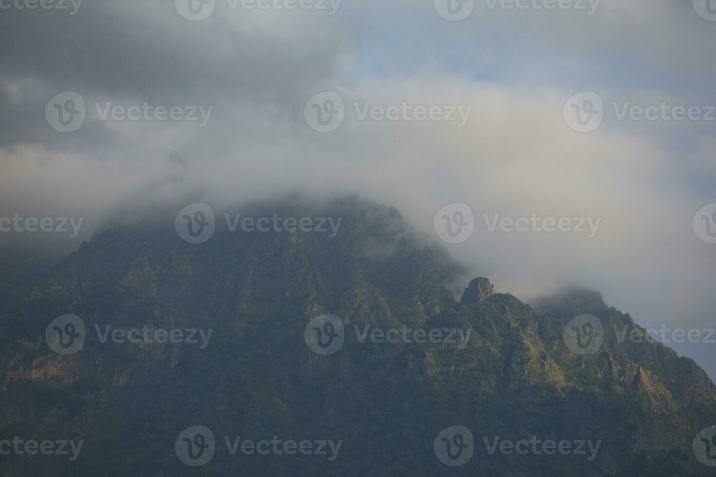 foncé atmosphérique surréaliste paysage avec une foncé rocheux Montagne de pointe dans faible des nuages dans une gris nuageux ciel. une gris faible nuage sur une haute culminer. haute noir Roche dans faible des nuages. surréaliste sombre montagnes. photo