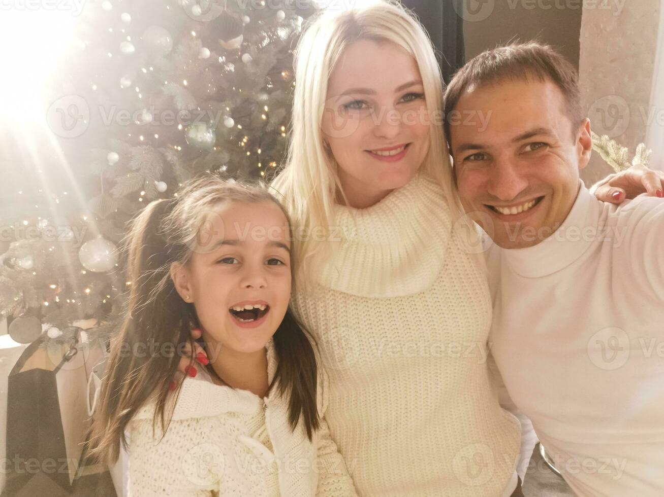 famille, vacances, La technologie et gens - souriant mère, père et peu fille fabrication selfie avec caméra plus de vivant pièce et Noël arbre Contexte photo