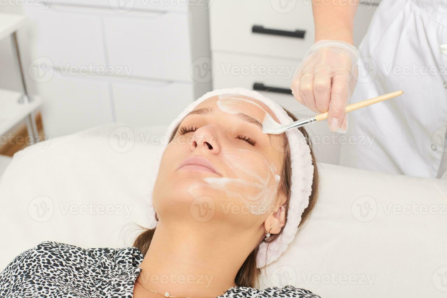 esthéticienne appliquant un masque de crème cosmétique sur le visage féminin pour une procédure de rajeunissement dans un salon de beauté photo