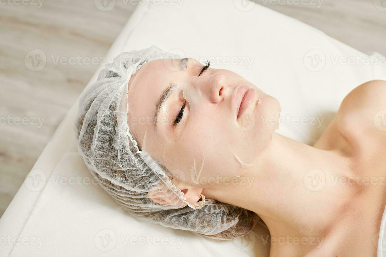 jeune femme en masque de feuille sur le visage pour réhydrater la peau du visage, procédure anti-rides dans un salon de beauté photo