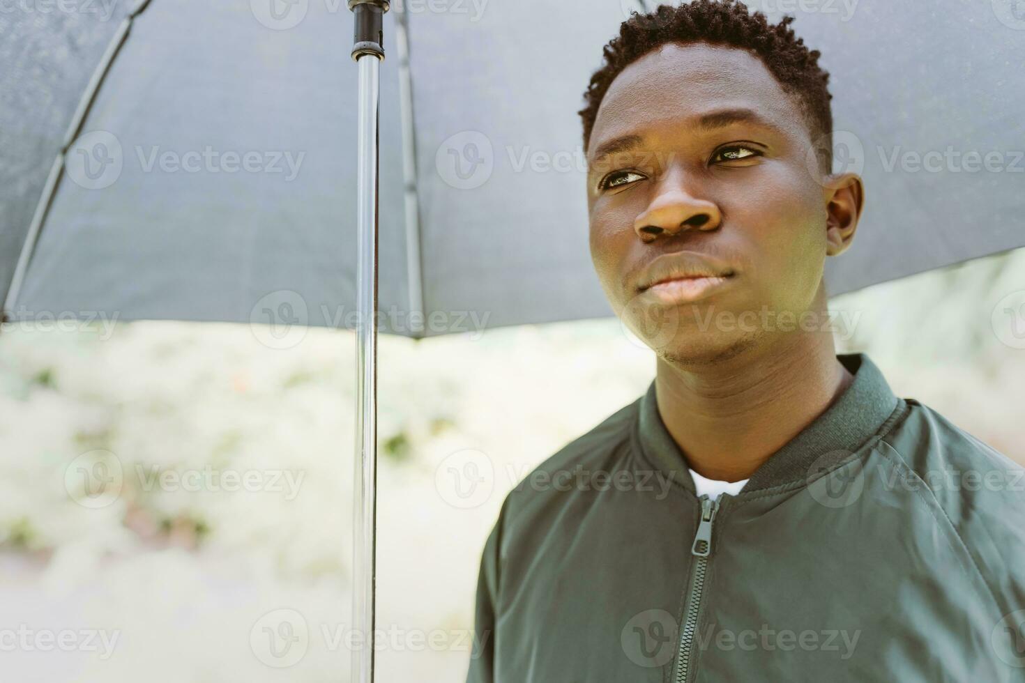 Jeune africain américain homme en dessous de noir parapluie dans pluie, triste. tomber ou printemps temps photo