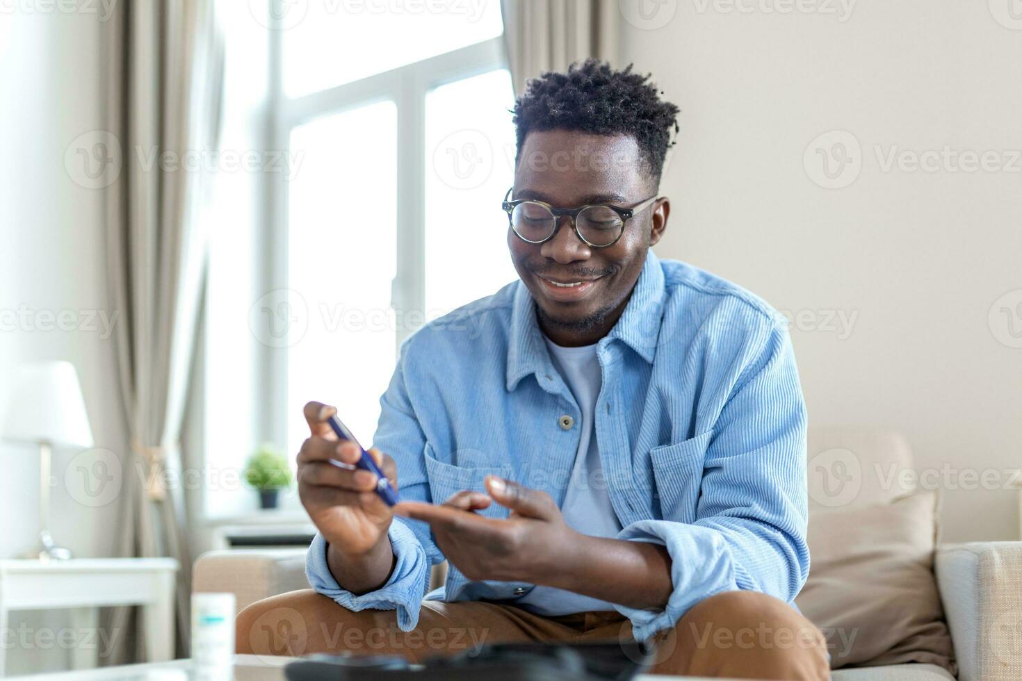 africain homme est séance à le canapé à le Accueil et prise du sang de le sien doigt dû à diabète. le du quotidien la vie de une homme de Afro-américain avec une chronique maladies qui est en utilisant glucose testeur. photo