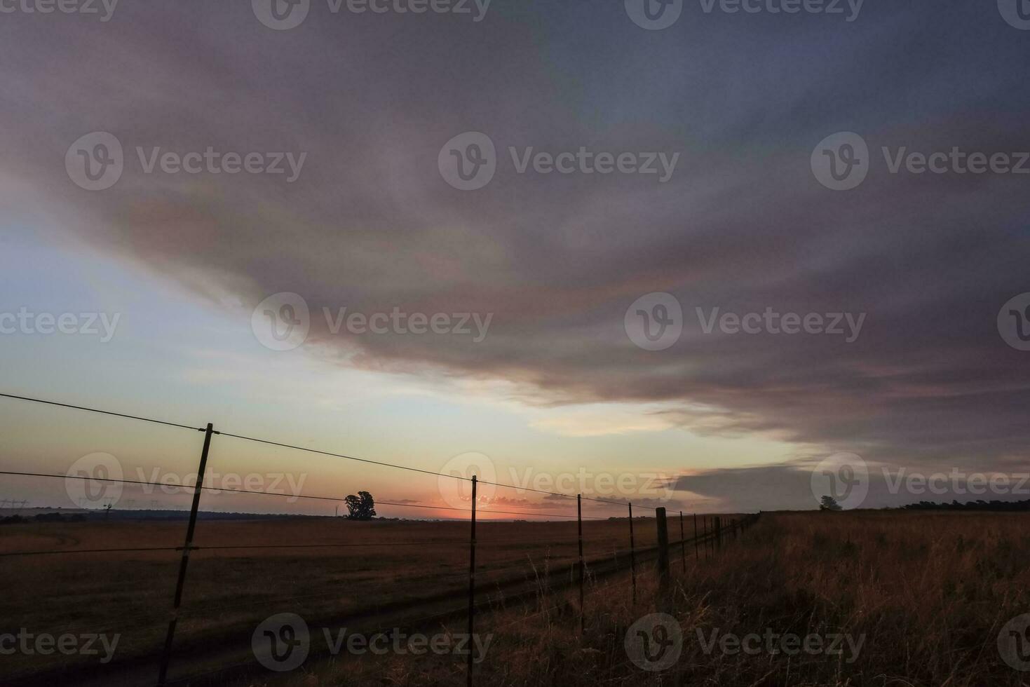 une le coucher du soleil plus de une champ avec une clôture et une clôture Publier photo