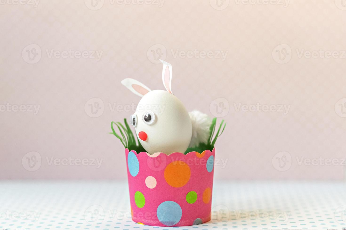 oeuf de poule blanc avec des oreilles de lapin et un museau dans un bac en papier rose respectueux de l'environnement, boîte. concept de joyeuses fêtes de pâques. photo