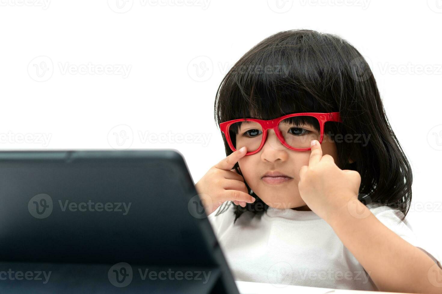 petite fille asiatique d'âge préscolaire portant des lunettes rouges et utilisant un tablet pc sur fond blanc, fille asiatique parlant et apprenant avec un appel vidéo avec une tablette, concept éducatif pour les écoliers. photo