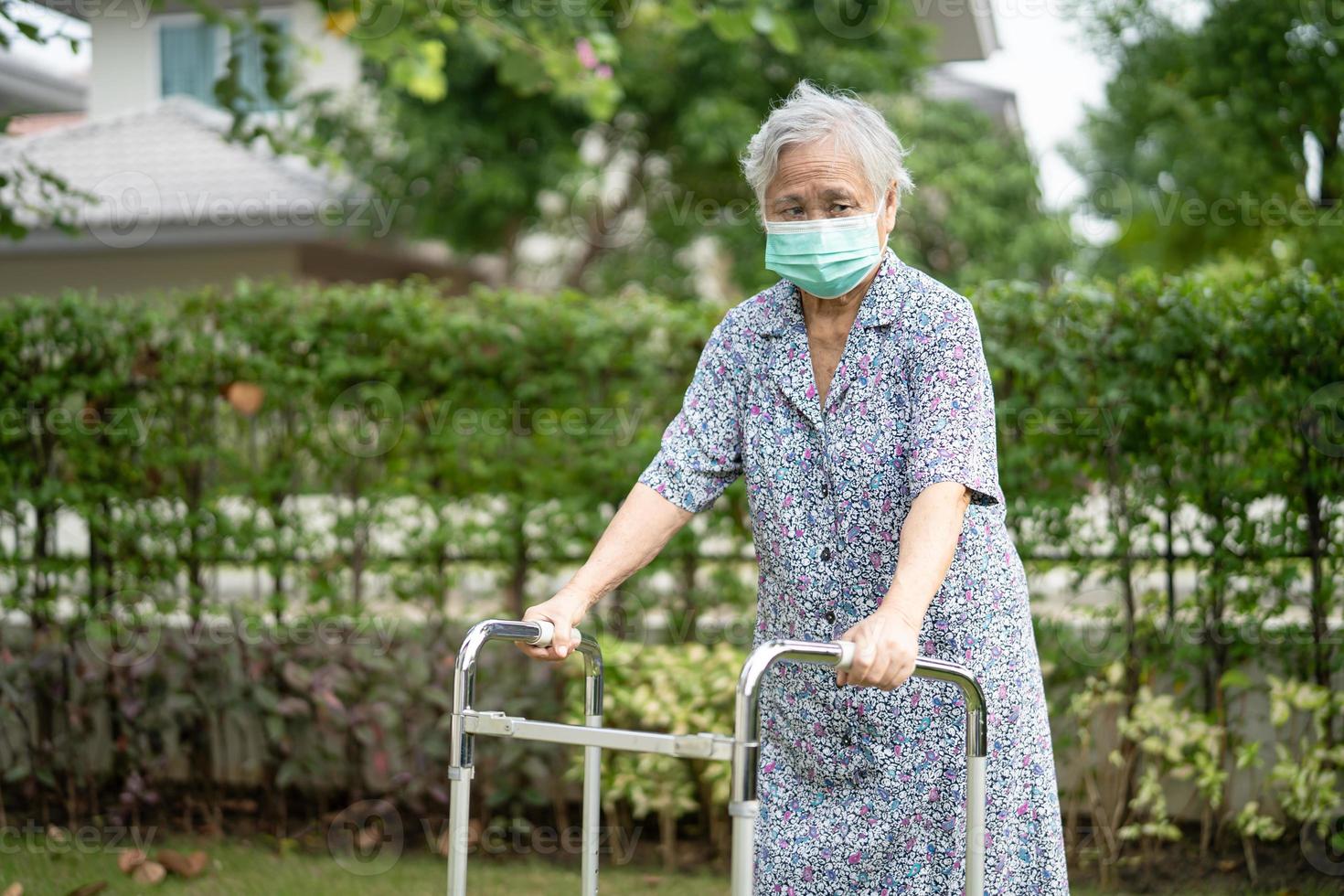 Une vieille dame asiatique âgée ou âgée marche avec un marcheur et porte un masque facial pour protéger l'infection de sécurité et tuer le nouveau virus du coronavirus covid-19. photo