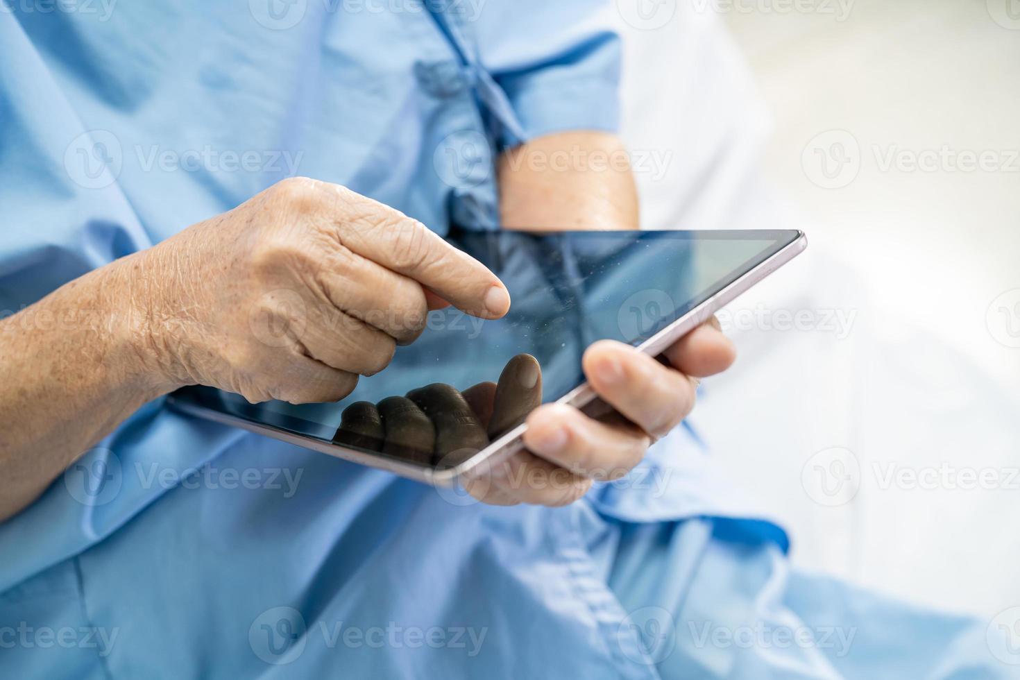 patiente asiatique âgée ou âgée tenant dans ses mains une tablette numérique et lisant des e-mails tout en étant assise sur son lit dans une salle d'hôpital de soins infirmiers, concept médical solide et sain photo