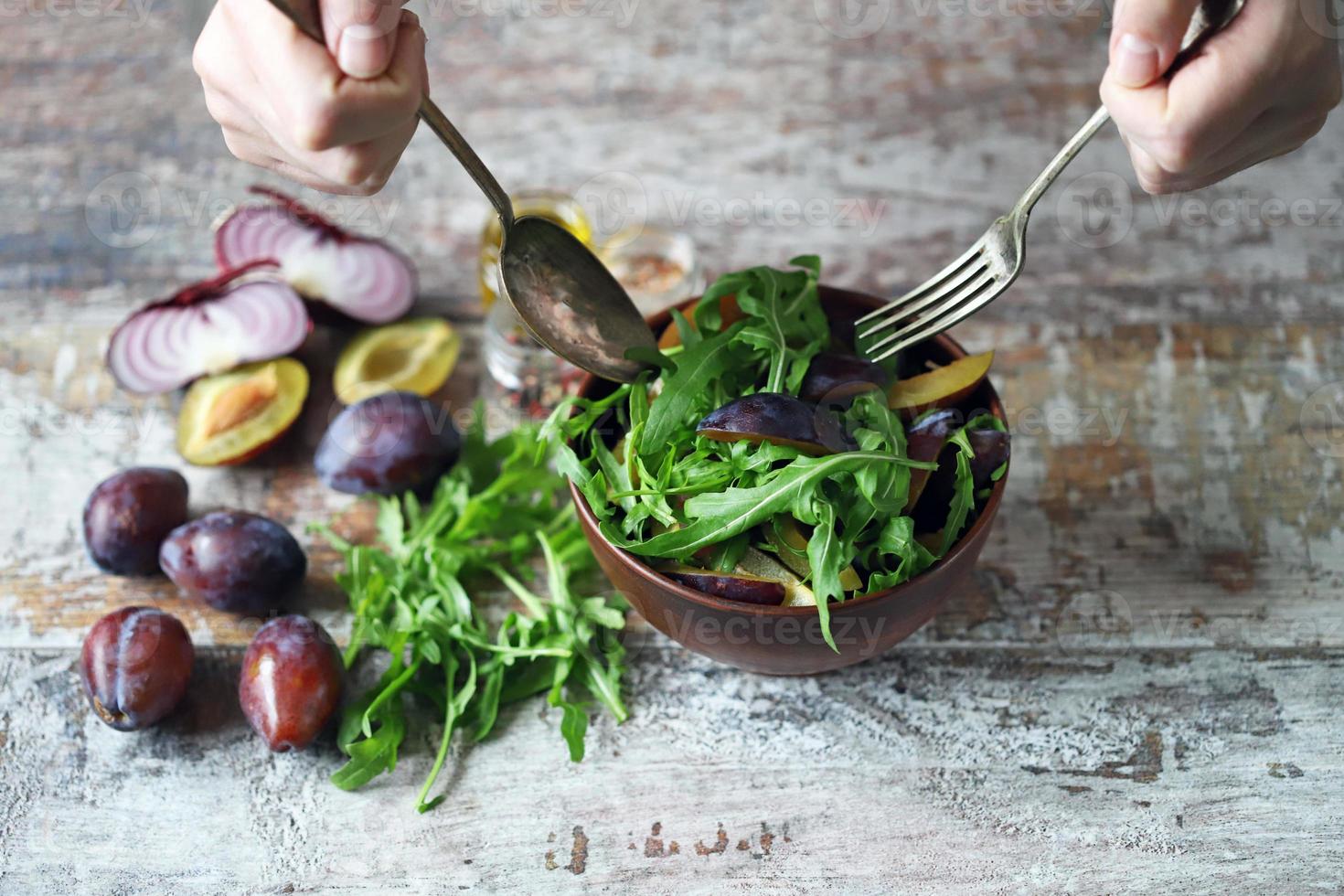 salade saine mélanger les mains des hommes avec une cuillère et une fourchette. salade de prunes de roquette. photo