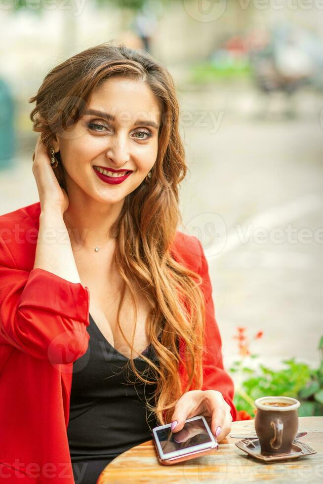 portrait de une Jeune blanc femme séance à le table avec une téléphone intelligent et à la recherche à caméra en plein air. photo