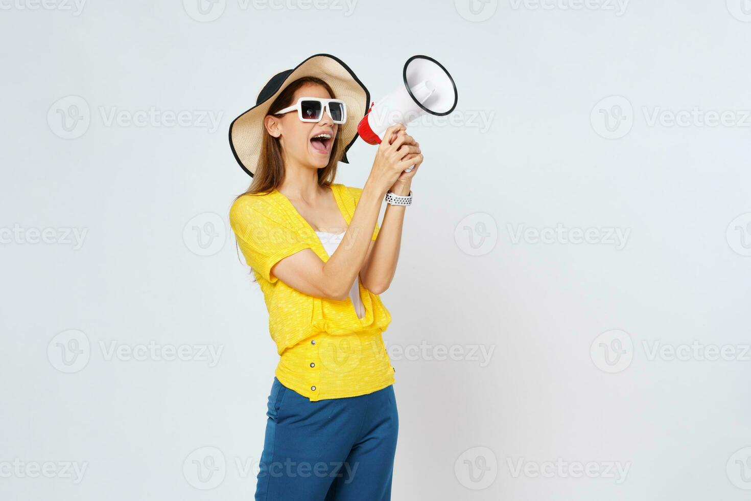 Jeune femme portant Soleil chapeau, des lunettes de soleil et en portant mégaphone isolé sur blanc Contexte. mode de vie été et annoncer concept. photo