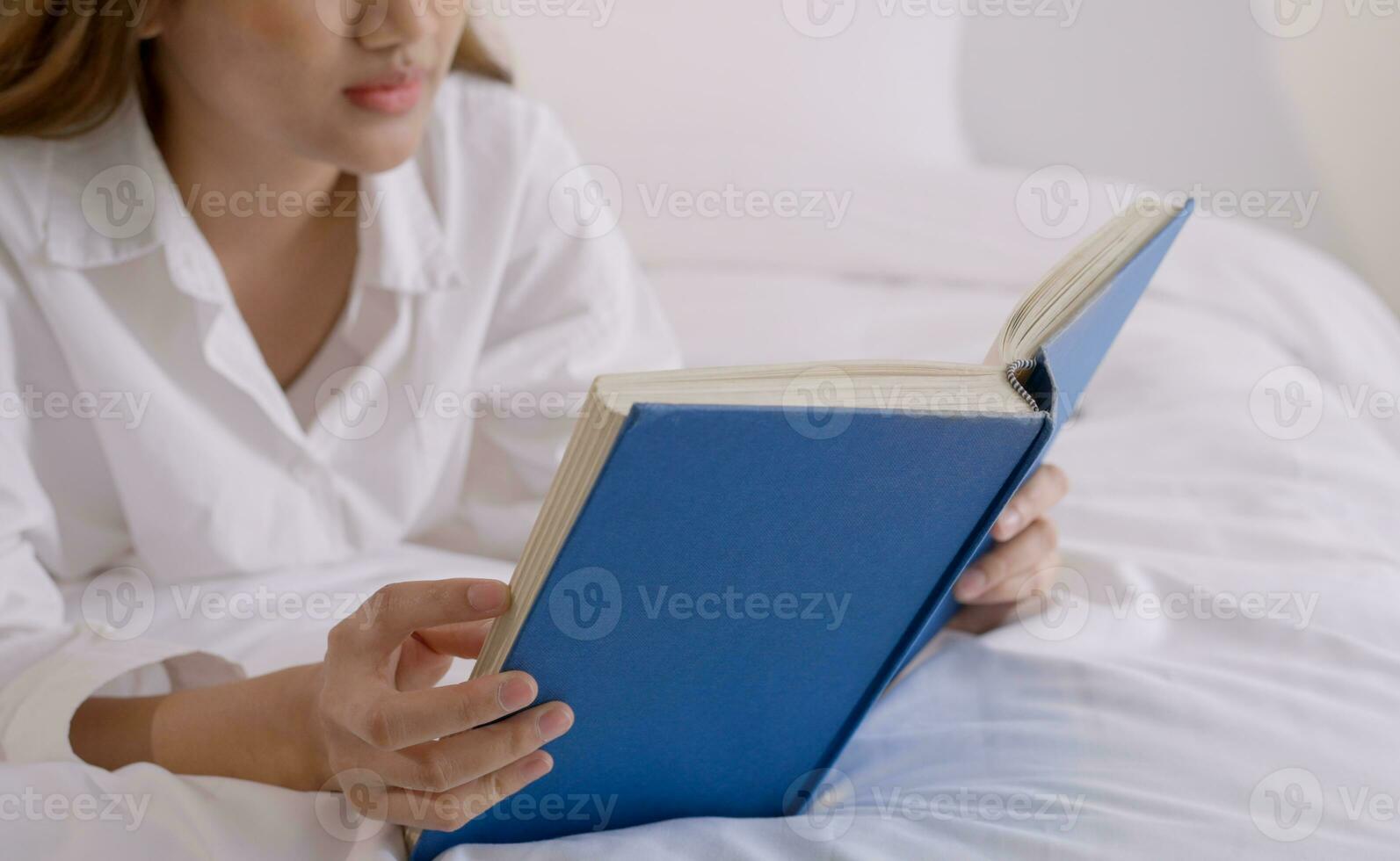 Jeune femme en train de lire livre sur lit à maison. photo