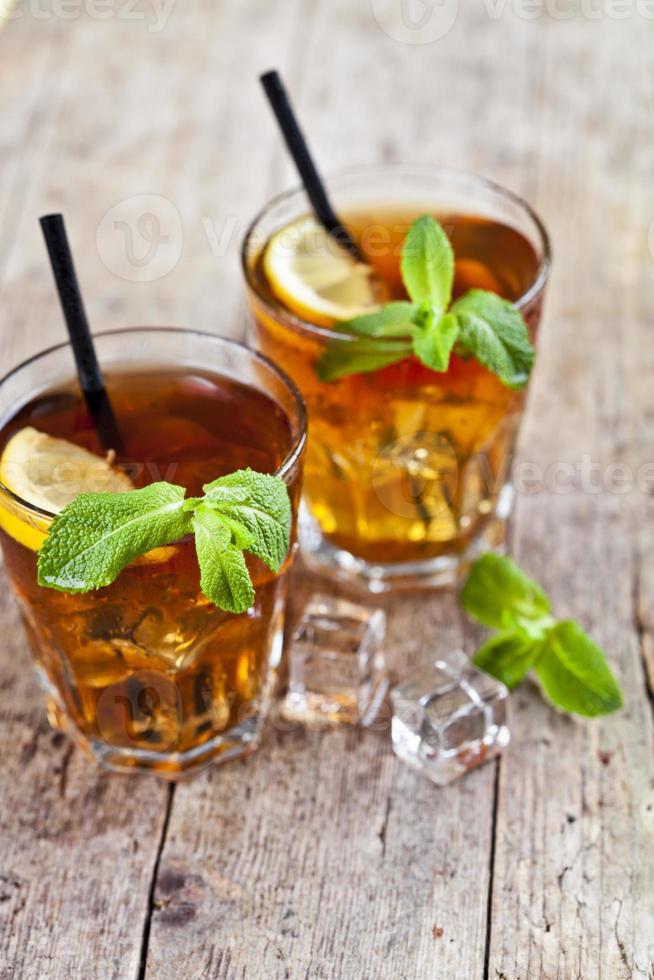 thé glacé traditionnel au citron, feuilles de menthe et glaçons dans deux verres sur une table en bois rustique. photo