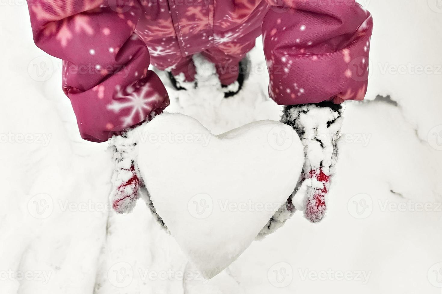 les mains des enfants dans des mitaines chaudes avec un cœur blanc comme neige fait de neige. le concept de la saint valentin photo