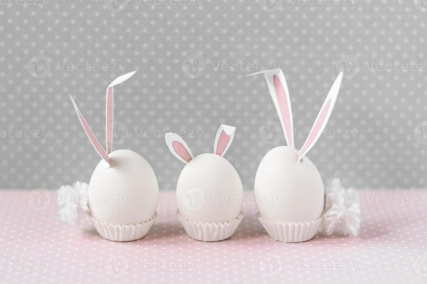 oeufs de poule blancs avec des oreilles et des queues de lapin sur fond de fleurs de lit. une famille. concept de joyeuses fêtes de pâques photo