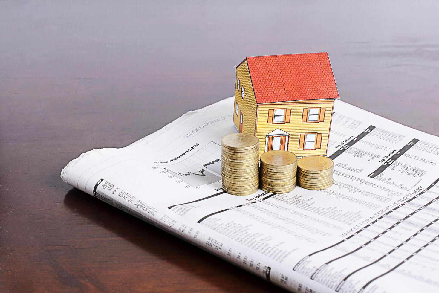 concept d'investissement immobilier avec maison en papier et pile de pièces sur papier journal sur table en bois photo