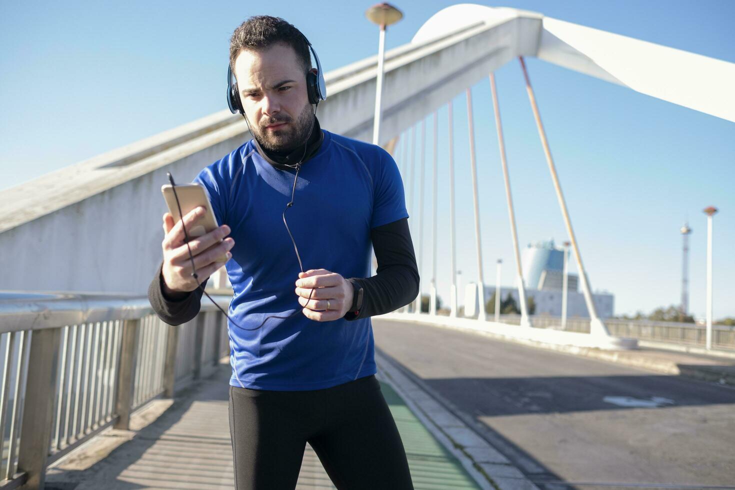 une fermer coup de une Masculin dans bleu écouteurs en utilisant le sien mobile tandis que le jogging dans le rue photo