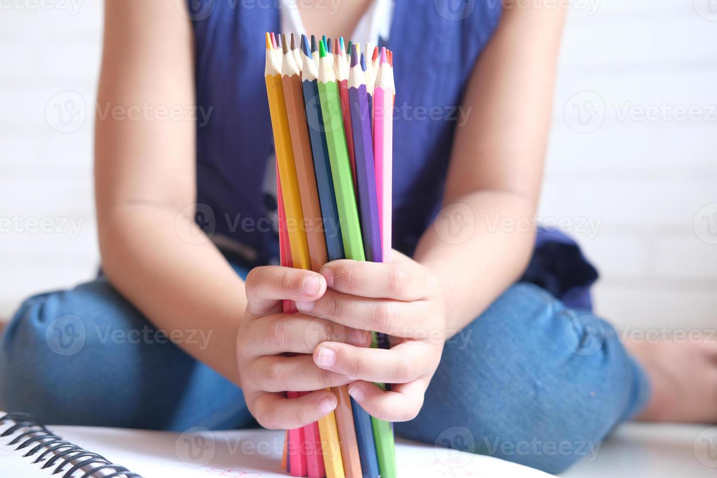 Fille enfant tenant de nombreux crayons de couleur assis sur le sol photo