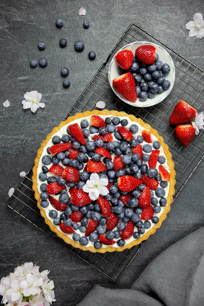 délicieux myrtille et fraise Tarte avec fouetté crème et mascarpone sur une foncé pierre Contexte. Haut voir. photo