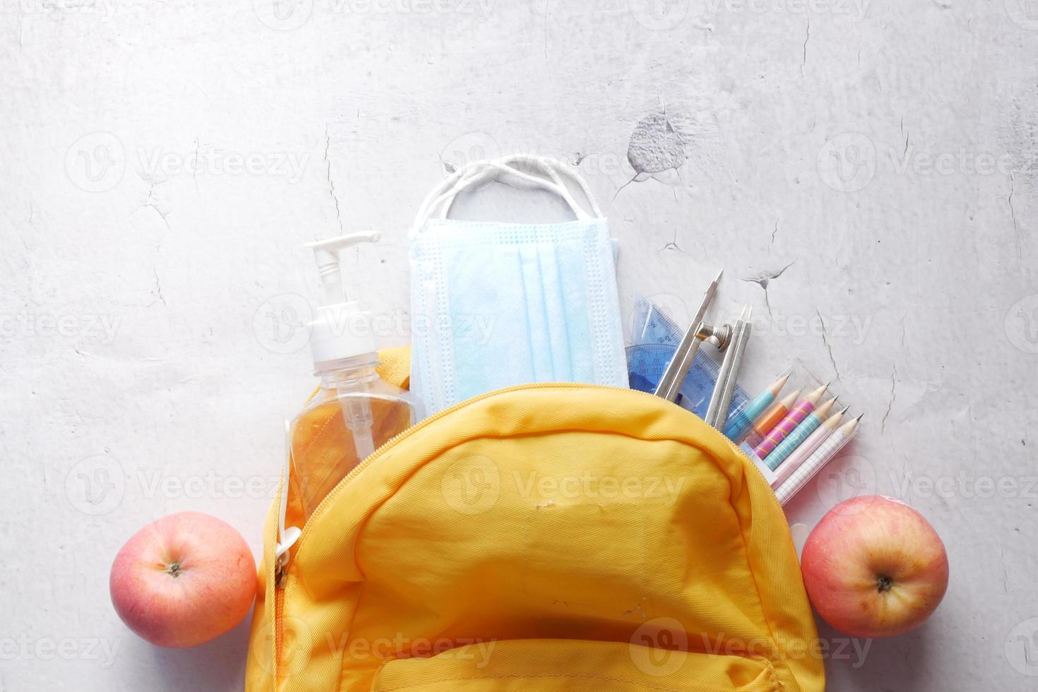 sac d'école étudiant avec désinfectant, un masque facial sur table photo