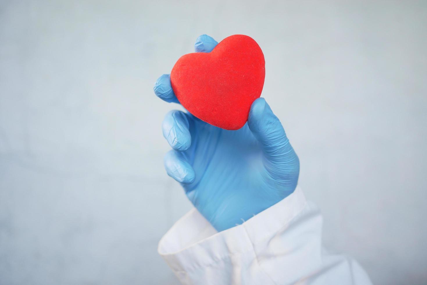 La main de l'homme dans des gants de protection tenant un coeur rouge sur fond blanc photo