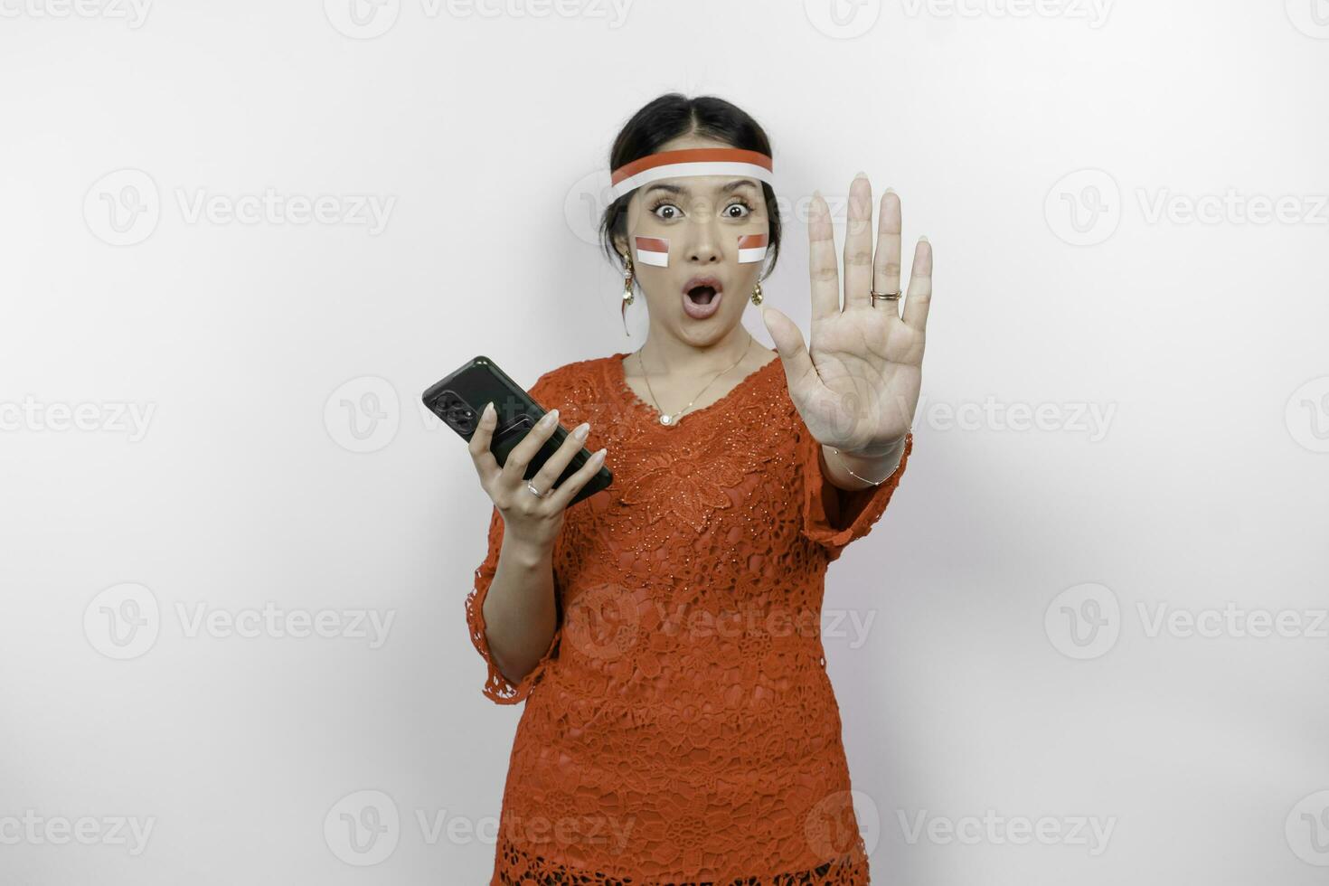 attrayant asiatique femme portant rouge kebaya et Bandeau avec main geste pose rejet ou interdiction tandis que en portant sa téléphone isolé par blanc Contexte photo