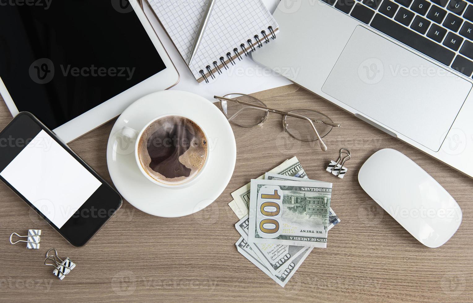 ordinateur portable avec des fournitures de bureau et de l'argent sur la table. photo