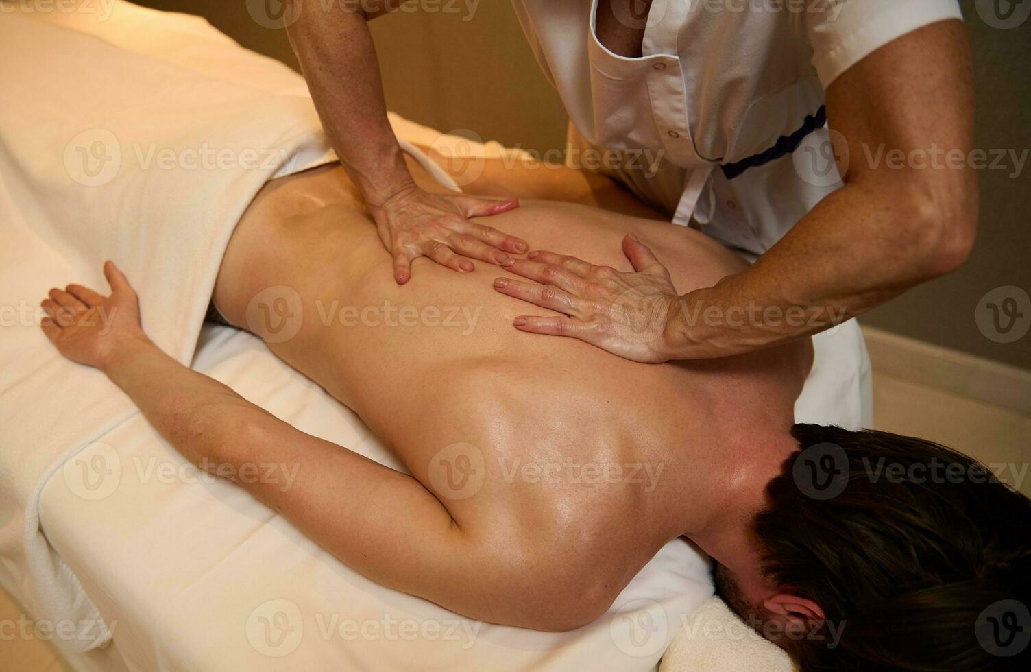ayurvédique traitement, professionnel thérapeutique corps massage à le bien-être spa clinique. une Jeune homme se détend tandis que mensonge sur une massage table pendant une thérapeutique retour massage à une luxe spa. photo