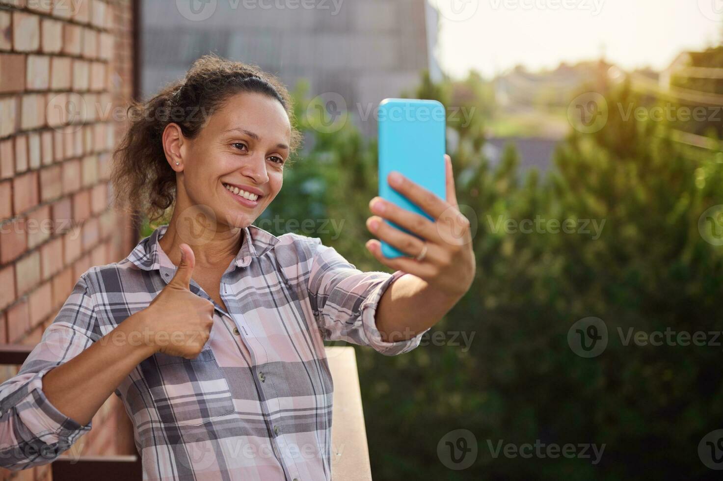 de bonne humeur femme montrant pouce en haut tandis que parlant par vidéo appel, permanent sur une balcon dans le campagne chalet photo