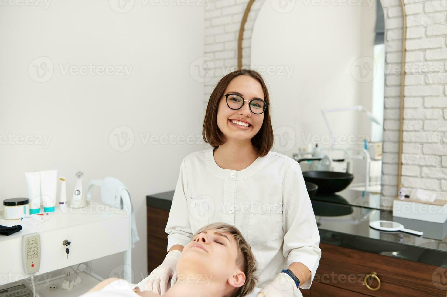 souriant cosmétologue séance près une client femme dans contemporain beauté spa clinique. photo