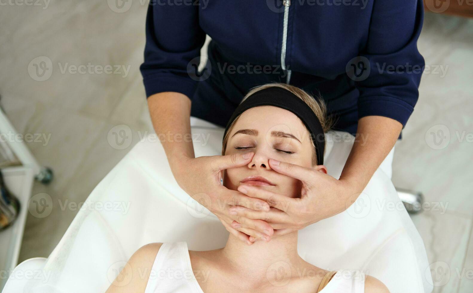 Haut vue de esthéticien Faire faciale anti-âge levage massage sur femme visage à spa clinique. professionnel lymphatique drainage massage à moderne spa centre photo