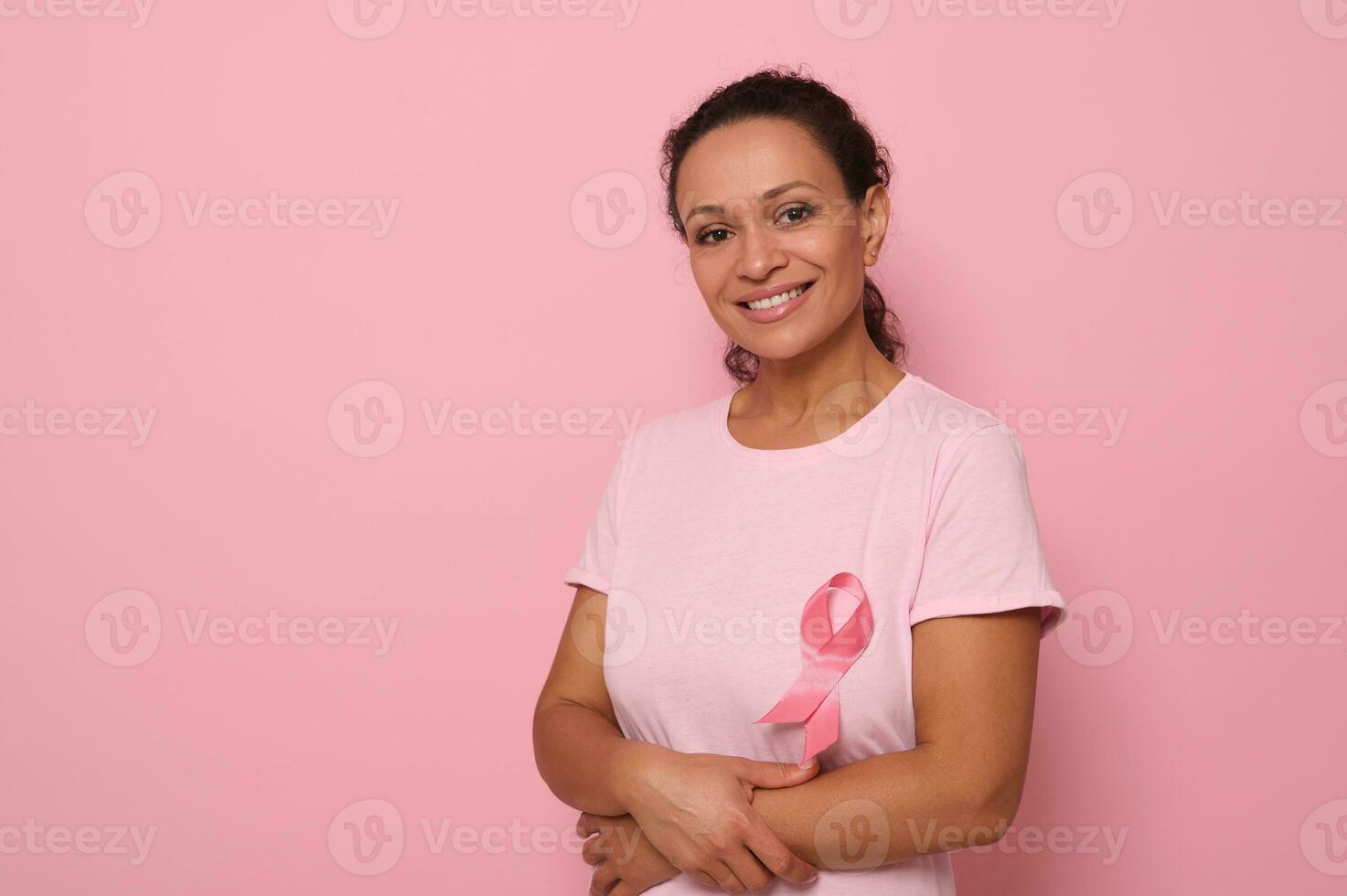 portrait de un altruiste, souriant mixte course femme dans une rose T-shirt avec une rose satin ruban, symbole de international Sein cancer journée. éducatif programme pour le bats toi contre cancer. 1 st octobre photo