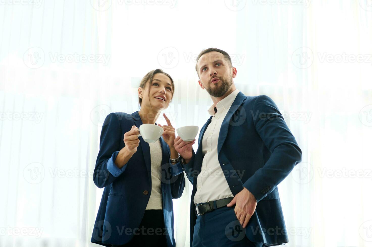 surpris affaires les partenaires, Bureau ouvriers, permanent avec une tasse de café à le fenêtre de une réunion chambre, hébété à la recherche à le côté, discuter quoi elles ou ils scie. diverse collègues à une café Pause photo