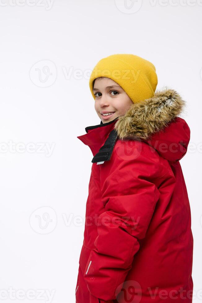 côté portrait de une Beau enfant, adorable préadolescent garçon dans brillant Jaune de laine chapeau et rouge vers le bas veste à la recherche par le sien épaule à caméra, isolé plus de blanc Contexte. copie un d espace photo