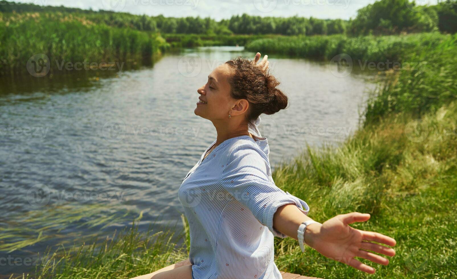 côté portrait de une content femme avec tendu bras profiter le beauté de le la nature sur le rivière Contexte photo