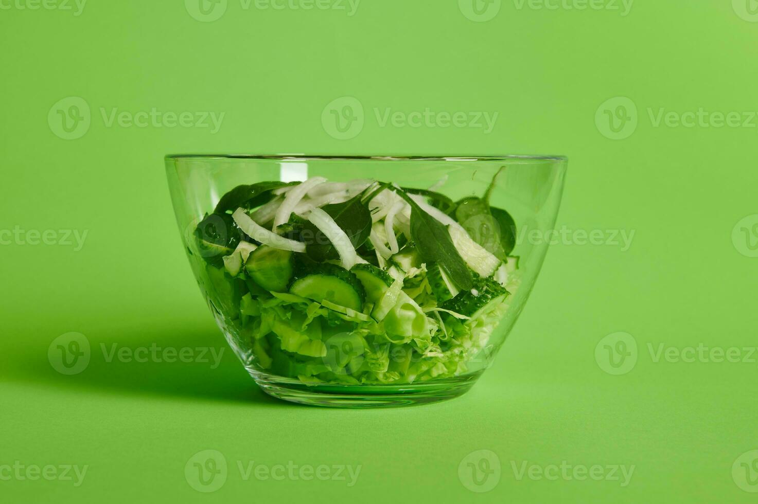 proche en haut de vert salade avec herbes, laitue, chou et concombre dans transparent verre bol sur vert Contexte photo